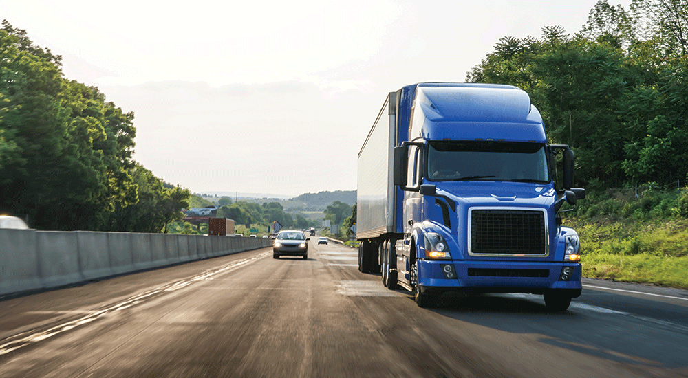 Blue truck driving on an asphalt road in a rural landscape